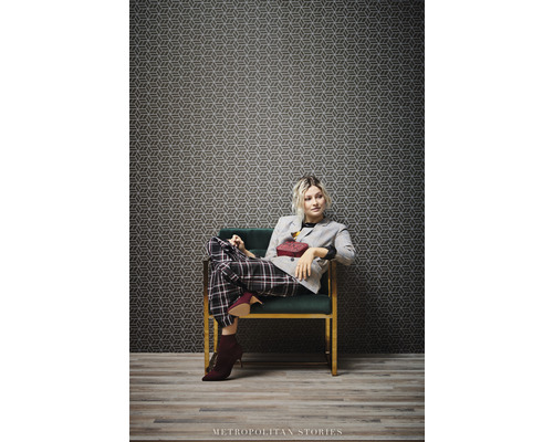 Žena sedí v kresle pred geometrickou vzorovanou tapetou