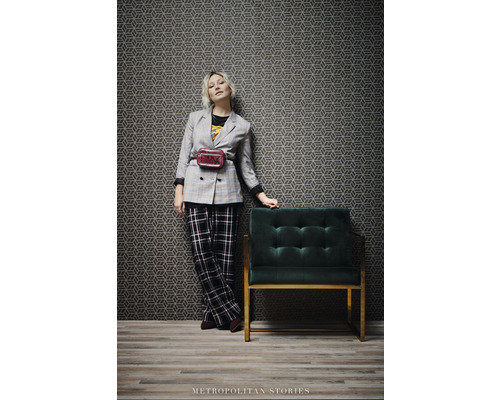 Žena v bunde a nohaviciach vedľa kresla a geometrickej tapety