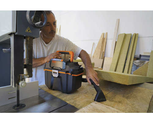 Remeselník používa mokro-suchý vysávač na dielenskom stole s pásovou pílou a zvyškami dreva