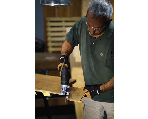 Muž používa priamočiaru pílu na rezanie kusa dreva. Nosí ochranné okuliare a rukavice.