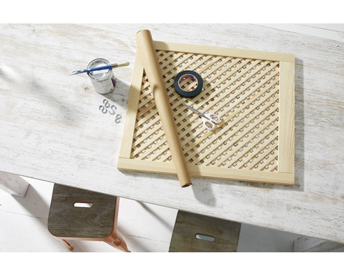 Drevený rám s mriežkou, plechovka farby, štetec, rolka papiera, izolačná páska a nožnice na stole