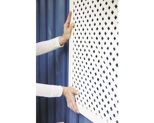 Osoba montuje bielu mriežku krytu radiátora s kosoštvorcovým vzorom