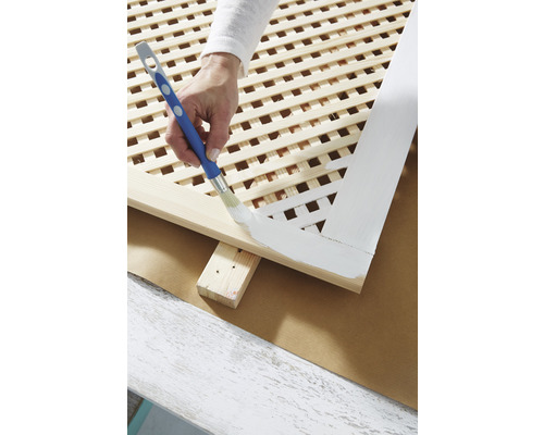 Osoba maľuje drevenú mrežu štetcom.