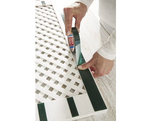 Osoba aplikuje lepiacu pásku Tesa na bielu mriežku.