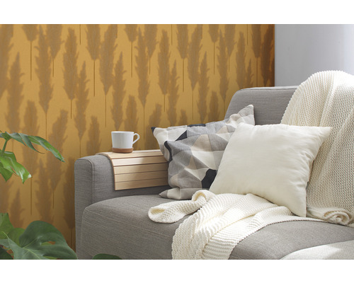 Sivá pohovka s vankúšmi a dekou, odkladací stolík s hrnčekom a vzorovaná tapeta