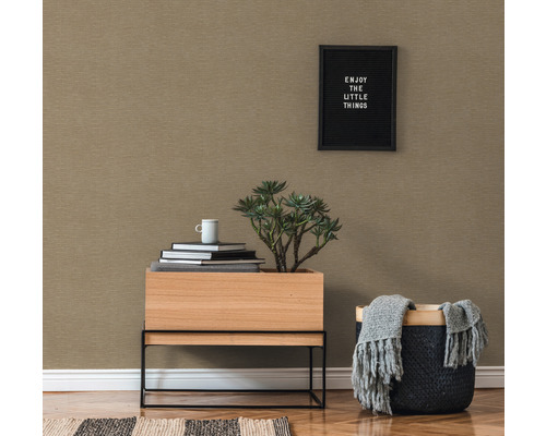 Detailný pohľad na miestnosť so vzorovanou tapetou, drevený stôl s rastlinou, hromada kníh a košík s dekou