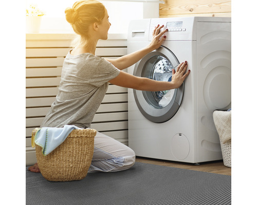 Žena obsluhuje práčku na sivej kúpeľňovej predložke
