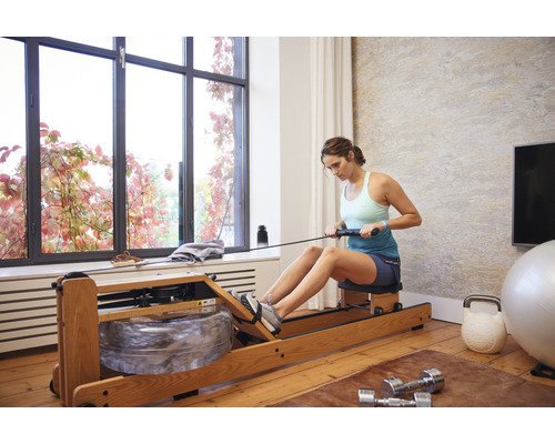 Žena používa veslovací trenažér vo svetlej miestnosti so športovým vybavením.