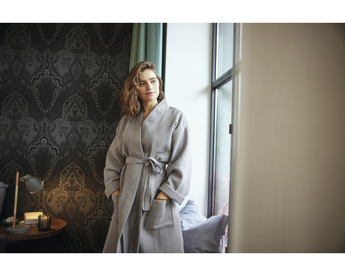 Žena v sivom vafľovom župane v izbe s tapetou so vzorom