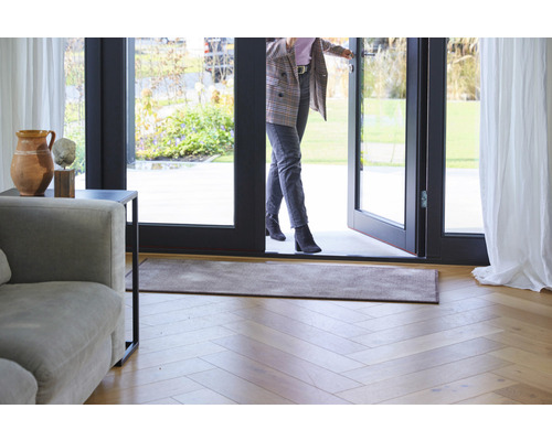 Vstupný priestor s rohožkou, drevenou podlahou a ženou prechádzajúcou dverami