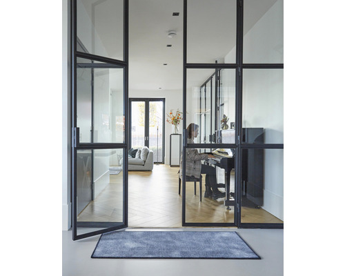 Interiérový záber obývacej izby so sklenenými dverami, kobercom a osobou hrajúcou na klavíri.