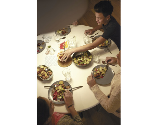 Rodina sedí za okrúhlym stolom a je šaláty a zemiaky.