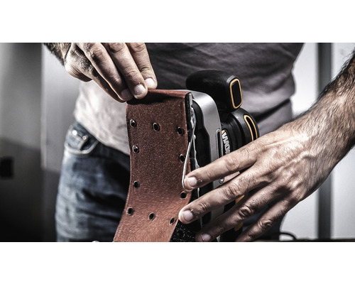 Osoba mení brúsny papier na pásovej brúske.