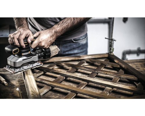 Osoba brúsi drevenú mriežku pomocou vibračnej brúsky.