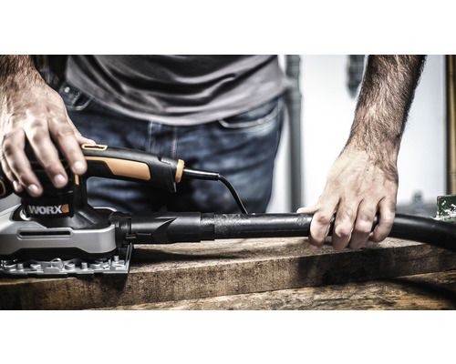 Muž brúsi drevenú dosku vibračnou brúskou značky Worx