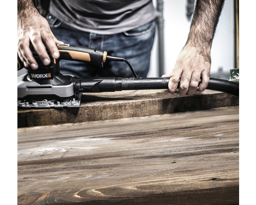 Muž brúsi drevenú dosku pomocou multifunkčnej brúsky s odsávaním prachu od firmy Worx
