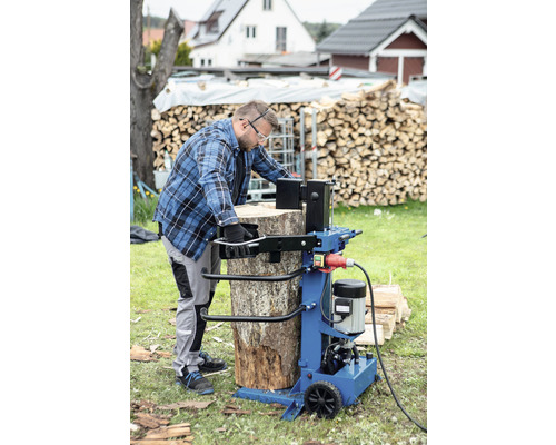 Muž štiepa poleno štiepačkou na drevo v záhrade.