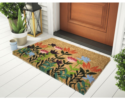 Kokosová rohožka s kvetinovým vzorom pred vchodovými dverami.