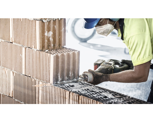 Murár reže tehlu pílou.