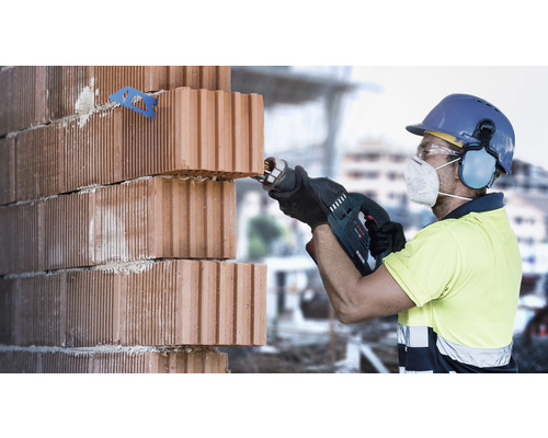 Stavebný robotník reže tehly mečovou pílou. Používajú sa osobné ochranné pomôcky.