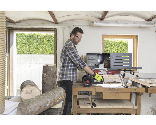 Muž pracuje so štiepačkou dreva v dielni. Polená ležia na stole.