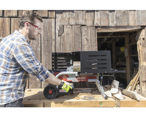 Muž obsluhuje štiepačku dreva AL-KO pred drevenou stenou.