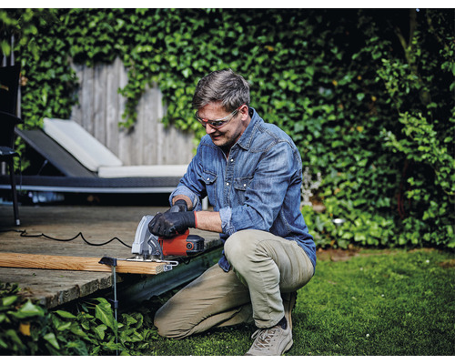 Muž pracuje v záhrade s ručnou kotúčovou pílou a má ochranné okuliare.