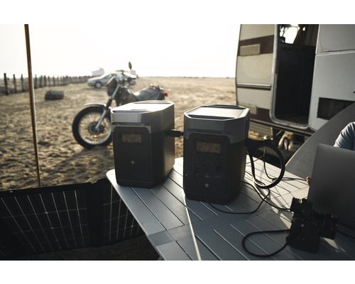 Scéna s dvoma generátormi elektriny na stole vonku s motocyklom, autom a karavanom v pozadí.