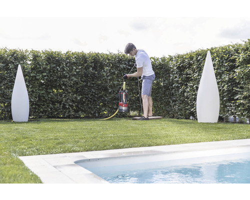 Muž obsluhuje kalové čerpadlo v záhrade blízko bazéna, po stranách sú dve dekoratívne svietidlá.