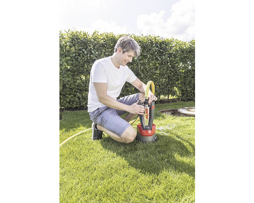 Muž kľačí na trávniku a pripája žltú hadicu k ponornému čerpadlu Al-Ko.