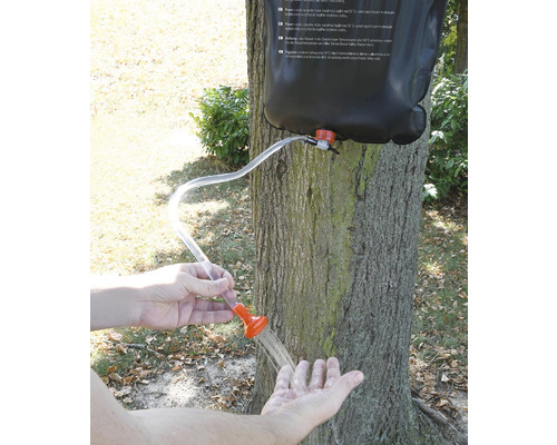 Prenosná sprcha s kvapkami vody v ruke pred stromom