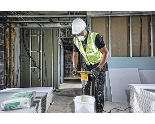 Stavebný robotník mieša tmel s miešadlom na stavenisku.