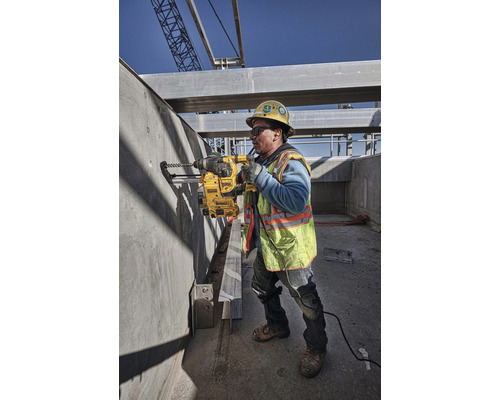 Stavebný robotník vŕta vŕtačkou otvor do betónovej steny na stavenisku.