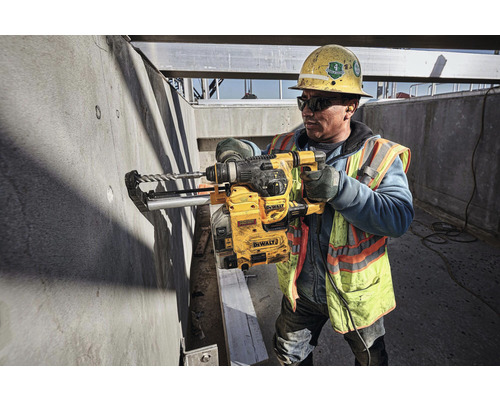 Stavebný robotník vŕta vŕtačkou DeWalt do betónovej steny na stavenisku.