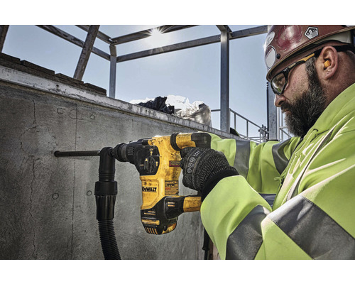 Stavebný robotník vŕta dieru do betónovej steny pomocou vŕtacieho kladiva DeWalt.