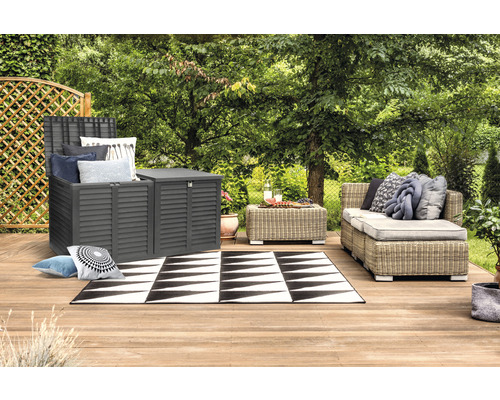 Záhradná scéna so sivou úložnou skriňou, ratanovou pohovkou a čierno-bielym kobercom na drevenej terase.