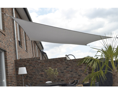Trojuholníková slnečná plachta nad terasou s tehlovou stenou a záhradným nábytkom