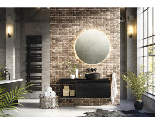 Moderná kúpeľňa s umývadlom, okrúhlym zrkadlom, radiátorom na uteráky a vaňou pred tehlovou stenou