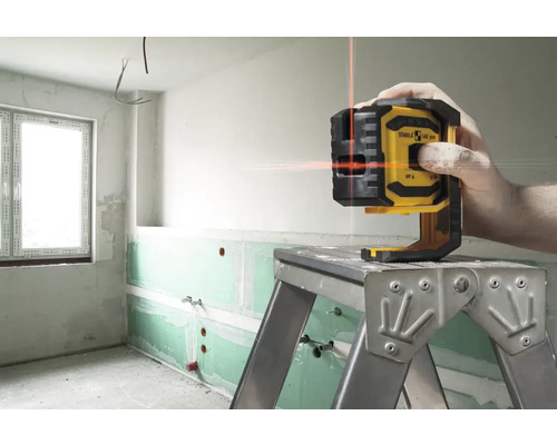 Logo Stabila. Krížový čiarový laser na rebríku v nezrekonštruovanej miestnosti s viditeľným vodovodným potrubím.