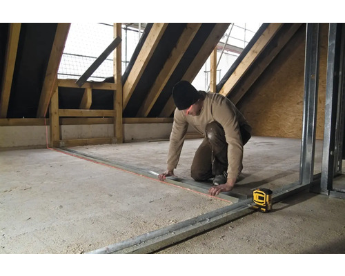 Remeselník pracuje s čiarovým laserom v podkroví na kovových profiloch.