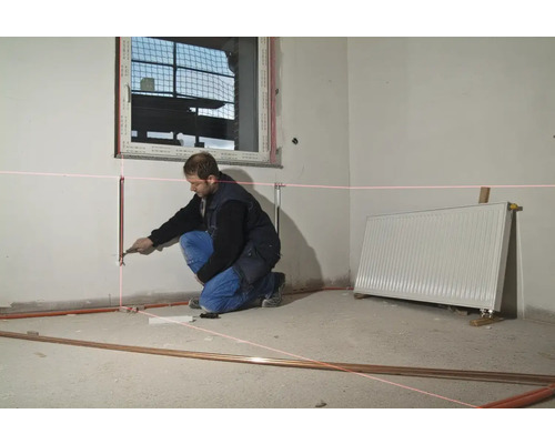 Remeselník nastavuje vykurovacie rúrky laserom v miestnosti.