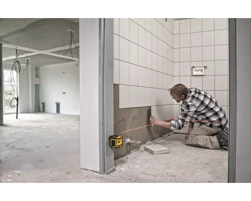 Muž kladie dlaždice pomocou čiarového lasera v nedokončenej miestnosti.