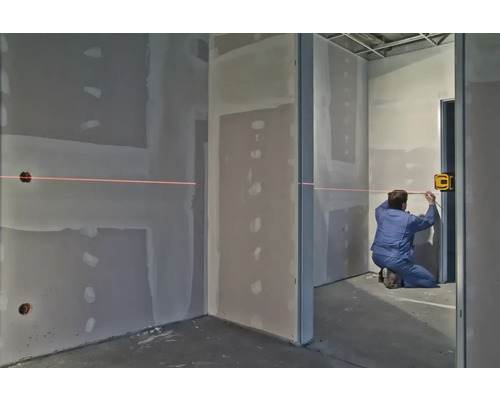 Muž používa krížový líniový laser v miestnosti so sadrokartónovými stenami na vyrovnanie.