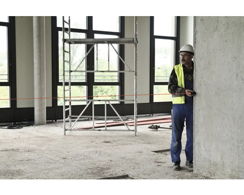 Stavebný robotník s laserovým diaľkomerom v hrubej stavbe s lešením