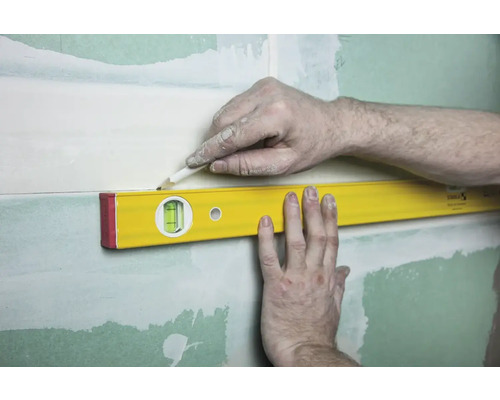 Na stenu so sadrou je pripevnená vodováha, osoba označuje čiaru ceruzkou.