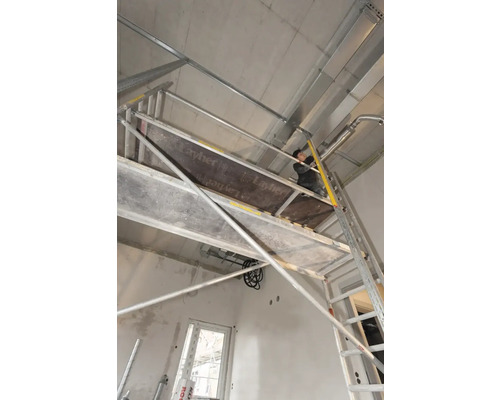 Pracovník na lešení vykonáva stropné práce v interiéri.