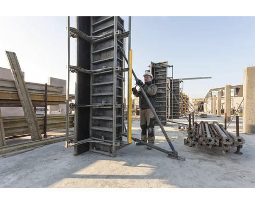 Stavebný robotník vyrovnáva betónové debnenie s vodováhou na stavenisku.