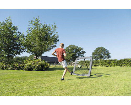 Chlapec kopne futbal do prenosnej futbalovej bránky v záhrade.