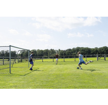 Tri deti hrajú futbal na trávnatom ihrisku s futbalovou bránkou.