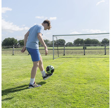 Mladík sa hrá s futbalovou loptou pred futbalovou bránkou v záhrade